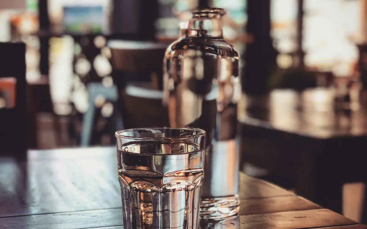 A glass of water and a clear bottle on a wooden table; illustrative stock photo